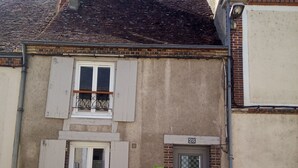 Un edificio de dos pisos con fachada de ladrillo, una ventana con contraventanas y una puerta con placa numérica.