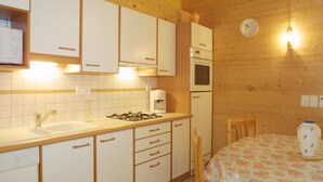 A compact kitchen with white cabinets, a gas stove, a microwave, and a sink. There is a wooden ceiling and a clock on the wall. - Charming 2-Bed Apartment, Wi-Fi, Near Ski Lifts & Center, Les Gets (Les Gets)
