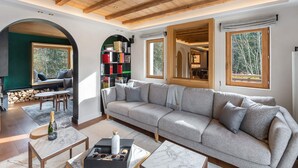 Ein gemütliches Wohnzimmer mit einem großen grauen Sofa, einer Holzbalkendecke und einem Bücherregal voller Bücher.