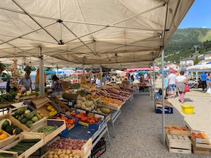 Un marché en plein air où divers étals proposent des produits frais, le tout abrité sous une grande marquise.