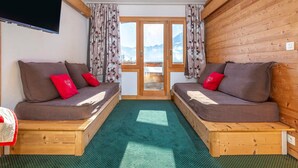 Quarto acolhedor com duas camas de madeira, uma TV na parede e vista para as montanhas pela janela.