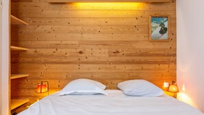 Cama com lençóis brancos e duas almofadas, com duas luminárias de cabeceira em prateleiras de madeira.