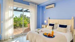 A bedroom with a bed, a nightstand, a window with curtains, and a balcony with plants. - Luxury Beachfront Villa with Private Terrace & Pools in Puerto Banús (Marbella)