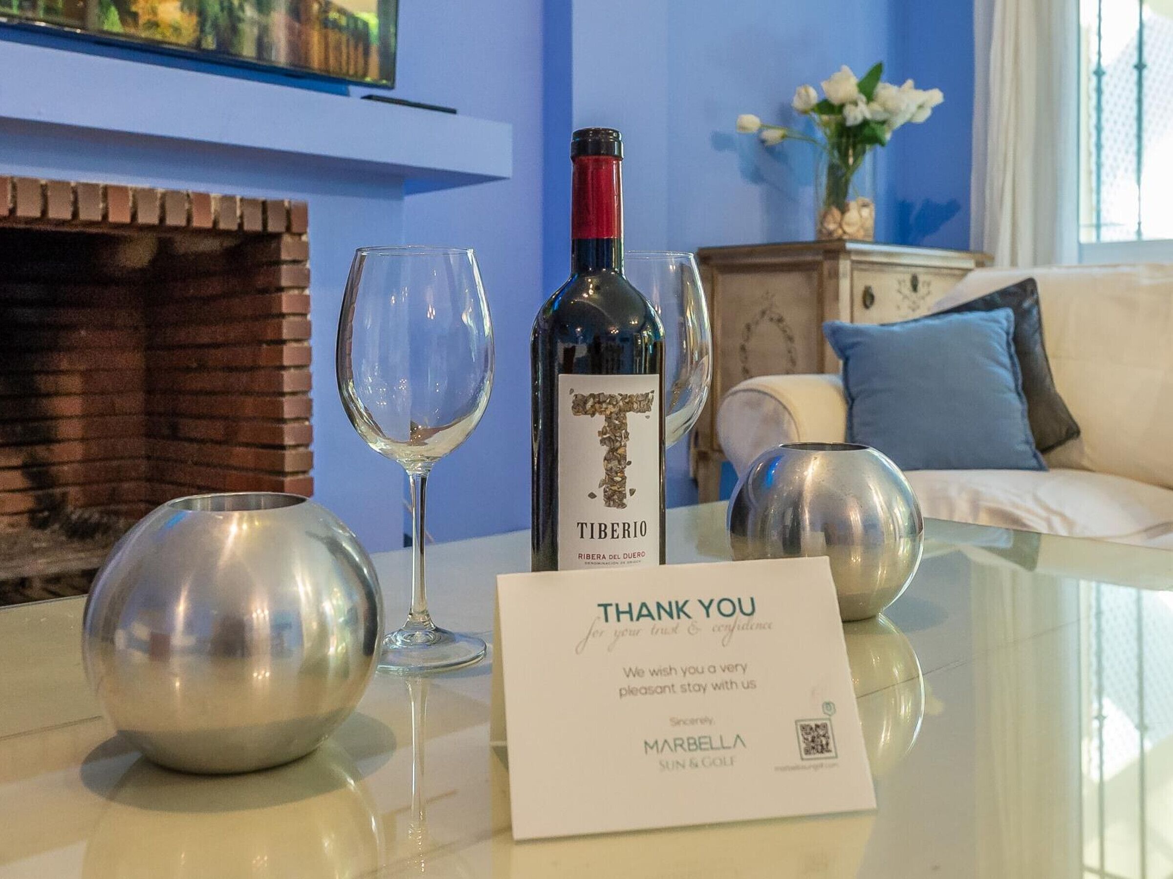 A table with a bottle of wine, two wine glasses, and a thank you card.