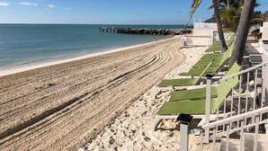 A beach with a row of green lounge chairs and a white fence. - P08 - Beautiful 4 bedroom, 3 bathroom half Duplex in Key Colony with private pool (Key Colony Beach)