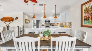 A dining area with a central island, white chairs, and a wooden table. - P08 - Beautiful 4 bedroom, 3 bathroom half Duplex in Key Colony with private pool (Key Colony Beach)