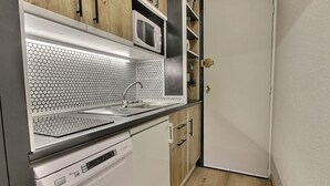 A compact kitchen with a dishwasher, a microwave, wooden cabinets, and a white door. - Renovated studio for 4 pers at the foot of the slopes (La Plagne)