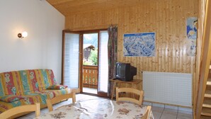 A wooden interior with a sofa, a table with a floral tablecloth, a television on a small table, and a poster on the wall. - Large apartment for 8, pets allowed, parking, near the slopes (Les Gets)