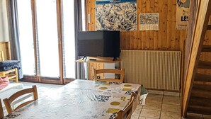 A wooden interior with a dining table, chairs, a television on a stand, and a poster on the wall. - Large apartment for 8, pets allowed, parking, near the slopes (Les Gets)