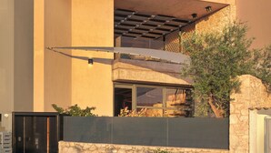 Un edificio moderno con fachada de piedra, un espacio al aire libre cubierto y una entrada protegida por una reja.