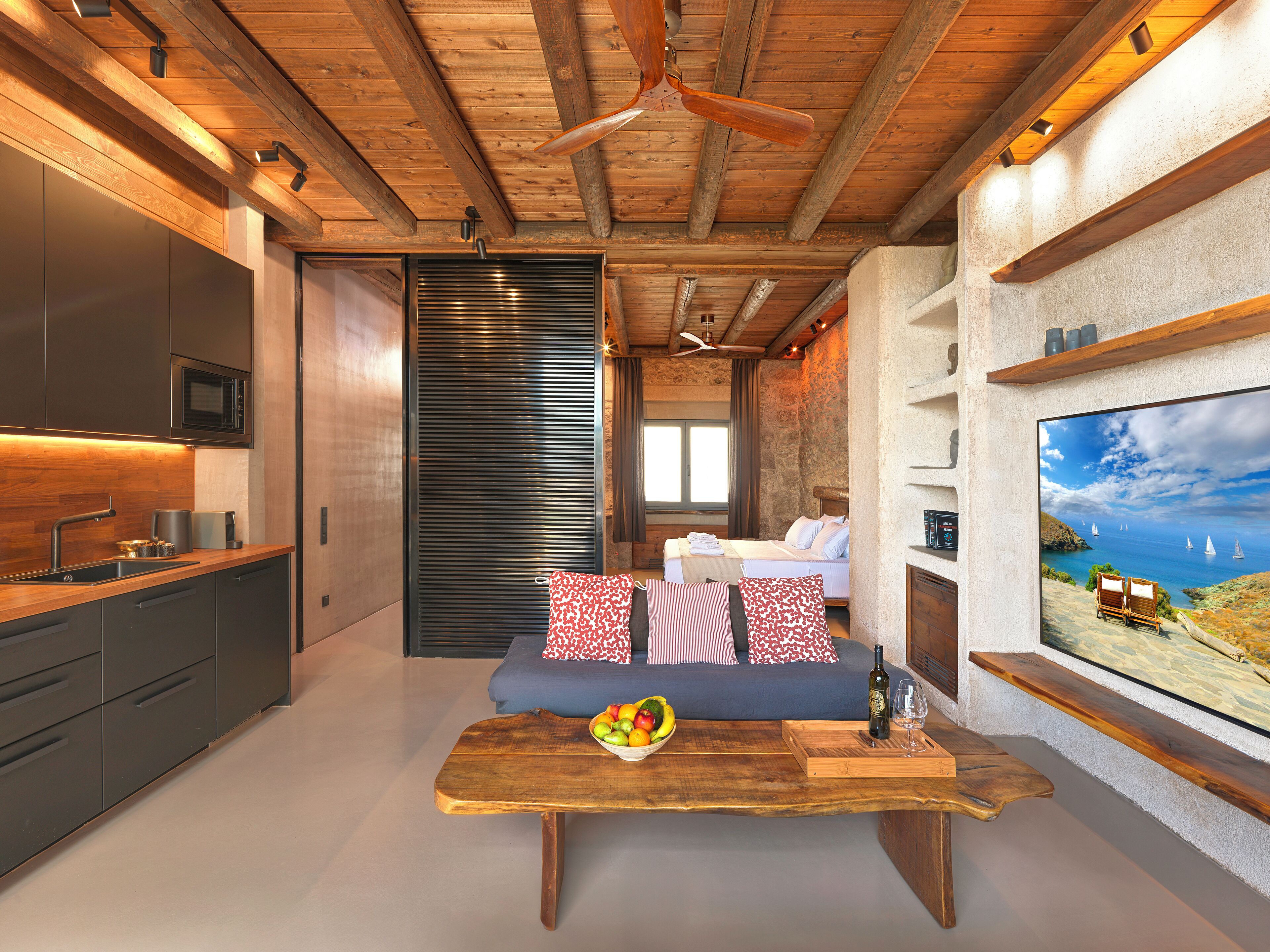 A modern interior with a wooden ceiling, a kitchen area, a seating area with a table, and a large TV screen displaying a scenic view.