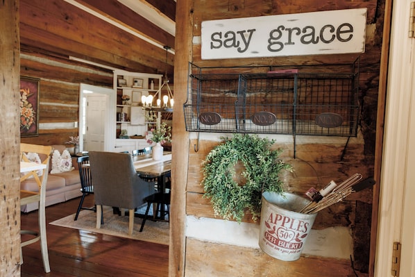 Un interior rústico con una pared de madera, un cartel que dice 'say grace' y un cubo etiquetado 'APPLES 50¢'.