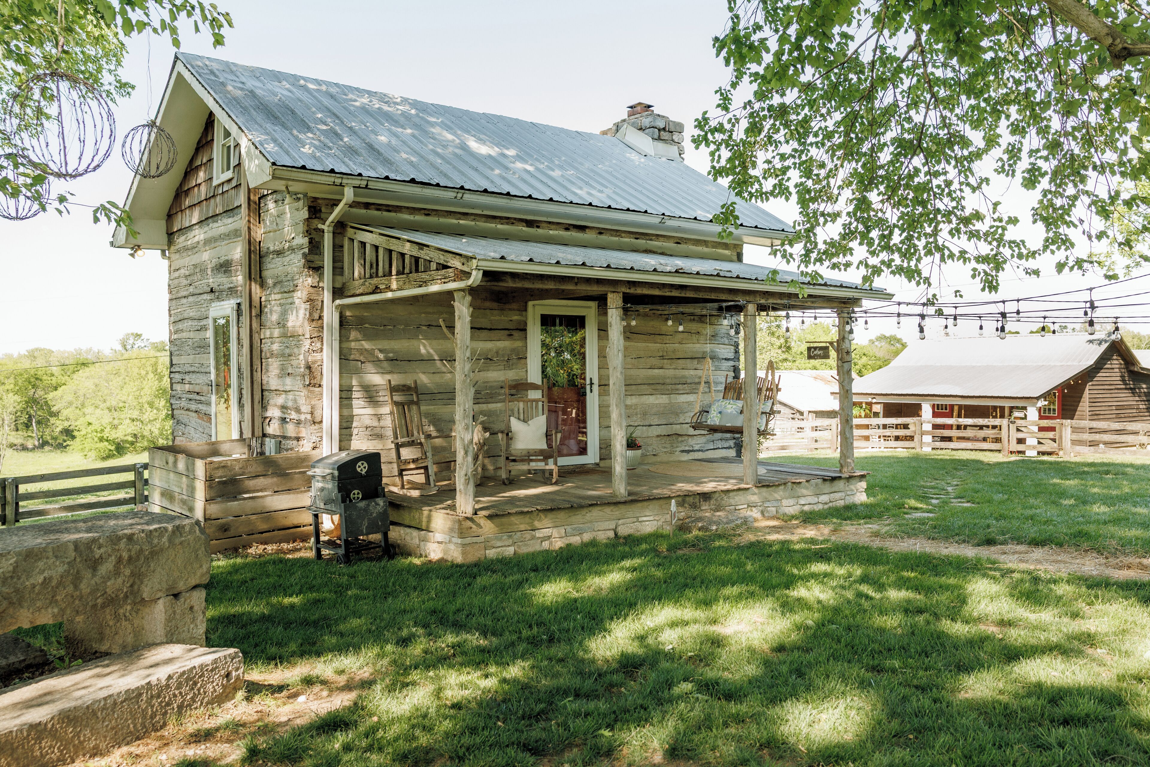 A rustic wooden cabin with a porch, stone steps, and a barbecue grill.