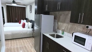 A compact hotel room with a bed, a kitchenette, a microwave, and a ceiling fan. - Myah's Luxury Suites Hotel (Diamond)
