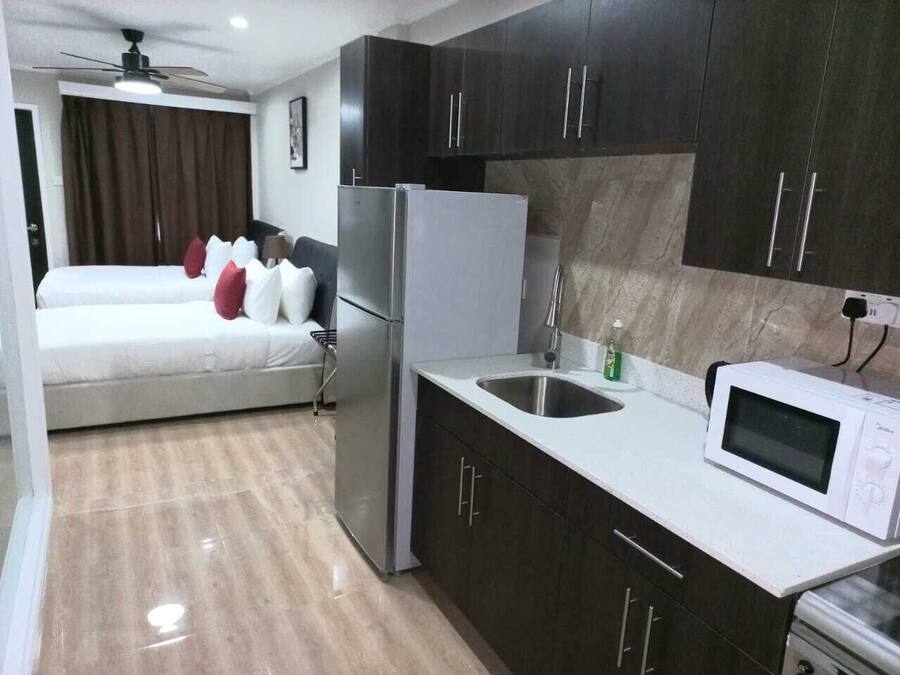 A compact hotel room with a bed, a kitchenette, a microwave, and a ceiling fan.