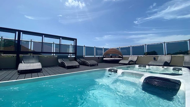 A rooftop pool with lounge chairs and a hot tub, surrounded by glass railings. - Myah's Luxury Suites Hotel (Diamond)