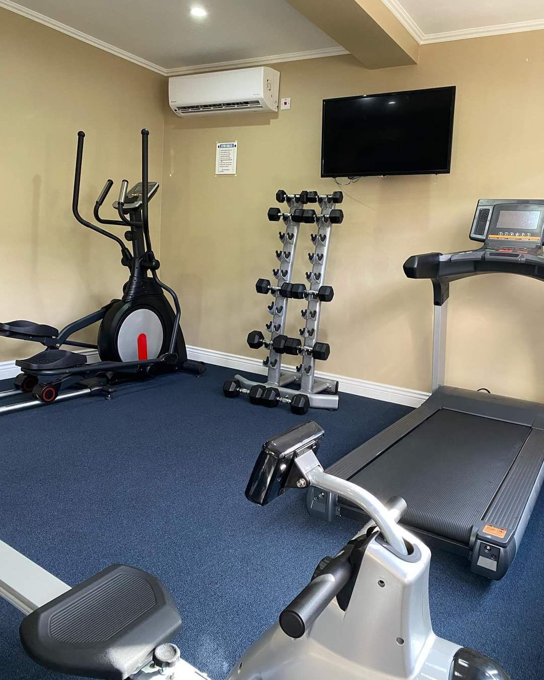 Une salle de sport équipée d’un tapis de course, d’un vélo elliptique et d’un banc de musculation.