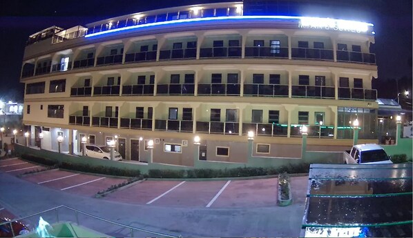 Un hotel de varios pisos con fachada curva, múltiples balcones y un estacionamiento al frente.