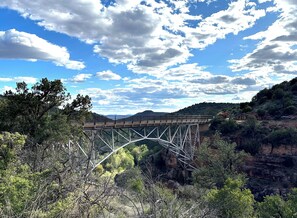 Eine Stahlbrücke mit einem Metallbogen über einem Canyons, umgeben von Bäumen und unter einem teils bewölkten Himmel.