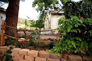 Un jardín con un columpio de cuerda, un muro de piedra y una casa al fondo.
