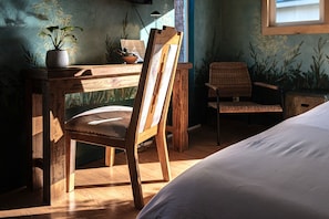 Un bureau en bois, une chaise, un lit et une fenêtre laissant entrer la lumière naturelle.