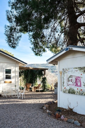 A rustic outdoor seating area with a table and chairs, a wooden pergola, and a building with a map and text on the side. - Professionally designed, centrally located to wineries and red rocks, premium bedding for a positive reset. Dogs Welcome. (Cornville)