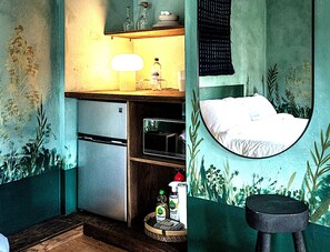 Een compacte kamer met een bed, een kleine kitchenette, een spiegel en een rond raam.