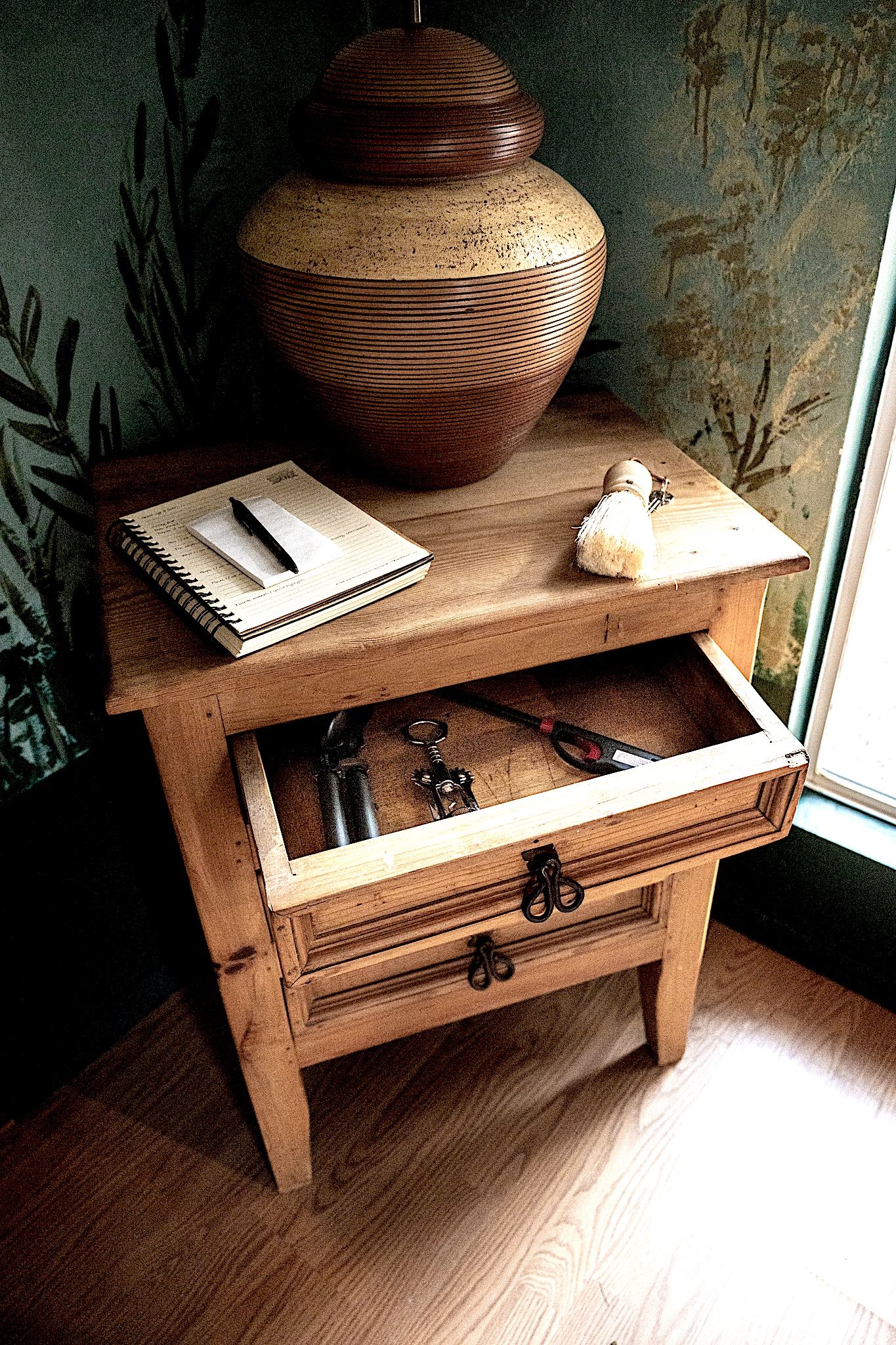Ein Nachttisch aus Holz mit einer Lampe, einem Notizbuch und Schlüsseln.