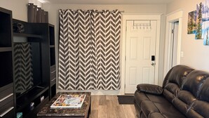 Una sala de estar con un sofá, una mesa de centro, un televisor y una cortina estampada.