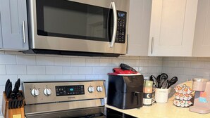 Una cocina con microondas, horno y estufa de acero inoxidable, además de una cafetera y un recipiente para utensilios.