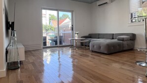 A spacious living room with a grey sectional sofa, a glass coffee table, and a sliding glass door leading to an outdoor area with a patio set. - Family Friendly Villa with Pool (Queens)