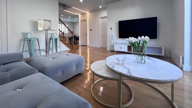 A modern living room with a grey sectional sofa, a marble coffee table, and a flat-screen TV mounted on the wall. - Family Friendly Villa with Pool (Queens)