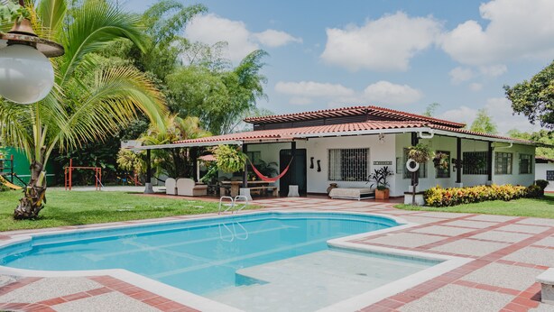 Una casa circondata da un giardino e palme, con una piscina.
