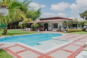 A house with a swimming pool, surrounded by a garden and palm trees.