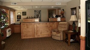 A living room with a wooden cabinet, a beige armchair, a small table with a lamp, and a plant. - Big Bend Traveler's Inn (Great Bend)