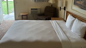 A hotel room with a large bed, a chair, a table, a lamp, and a painting on the wall. - Big Bend Traveler's Inn (Great Bend)