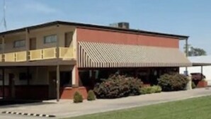 A two-story building with a flat roof, a covered front porch, and a parking lot with cars. - Big Bend Traveler's Inn (Great Bend)