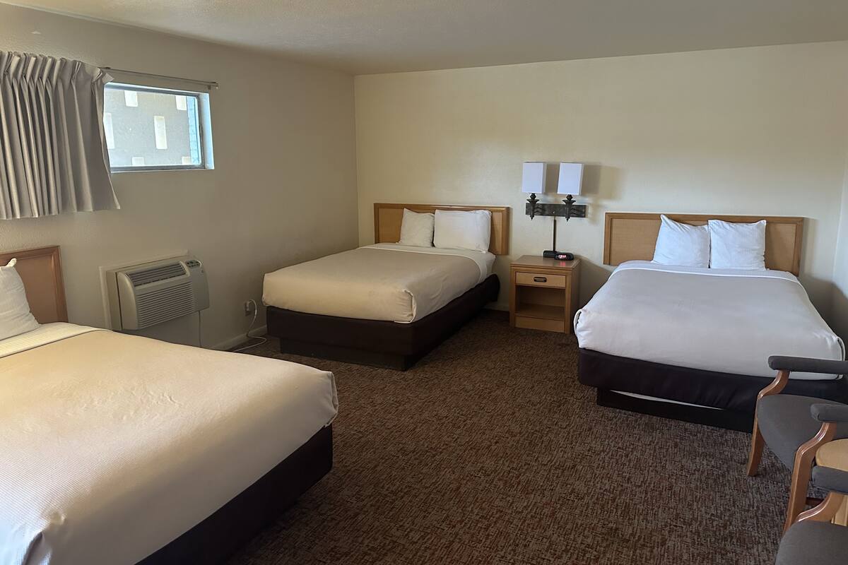A hotel room with two single beds, a nightstand with a lamp, a heater, and a window with curtains.