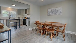 A modern kitchen with a dining area, featuring a wooden table and chairs, a large window, and a hanging light fixture.