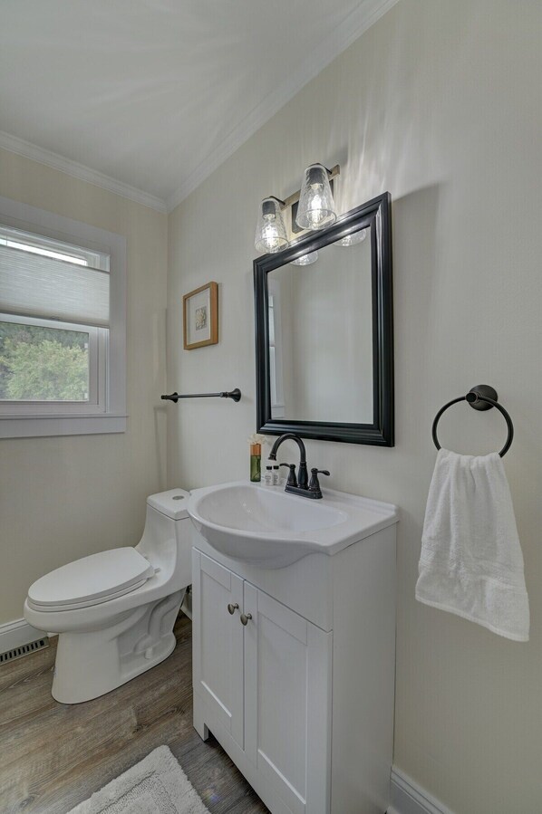Une salle de bain avec des toilettes blanches, un lavabo blanc avec un robinet noir, un miroir avec éclairage intégré et un porte-serviettes.
