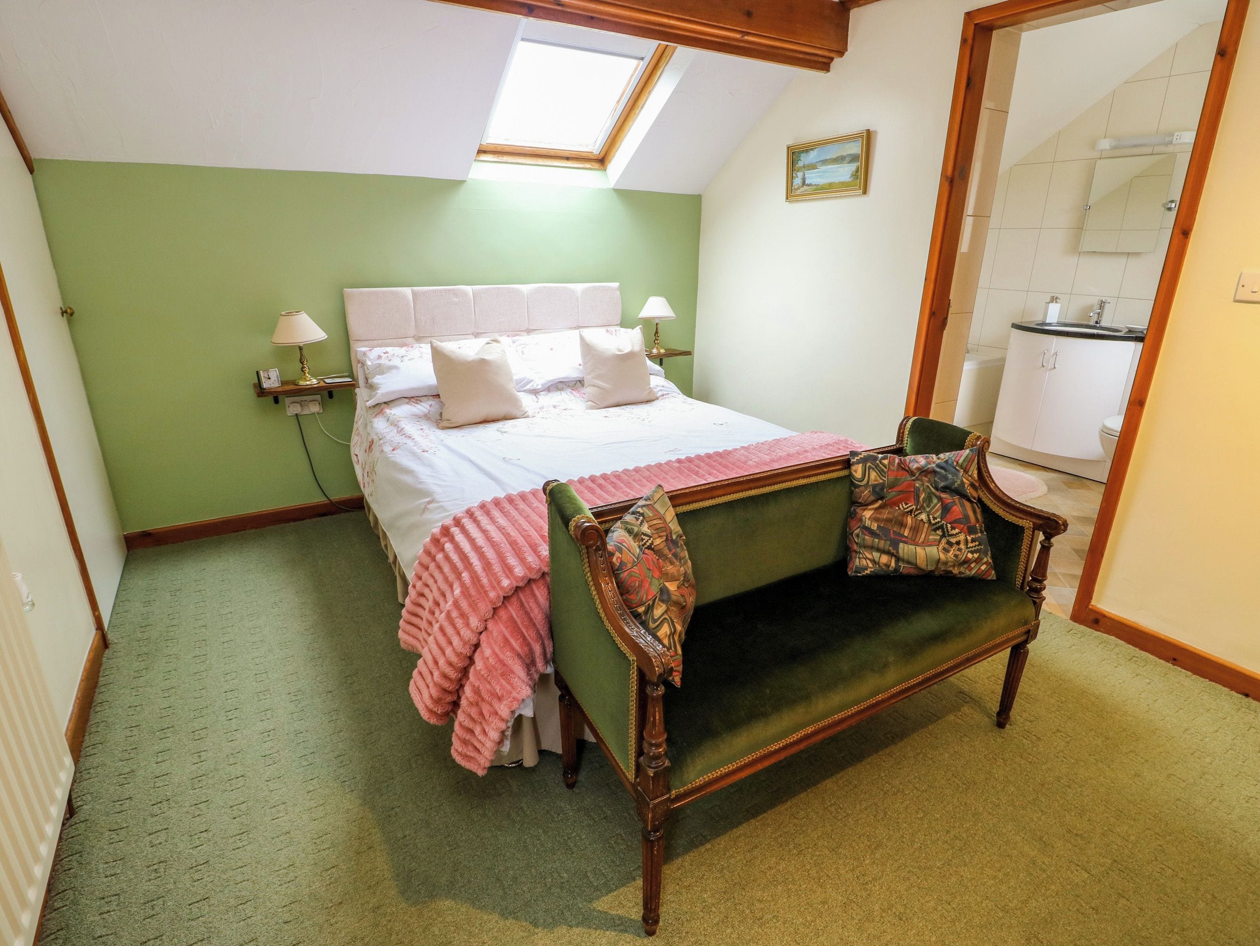 A bedroom with a bed, bedside lamps, a green armchair, a mirror, and a skylight.