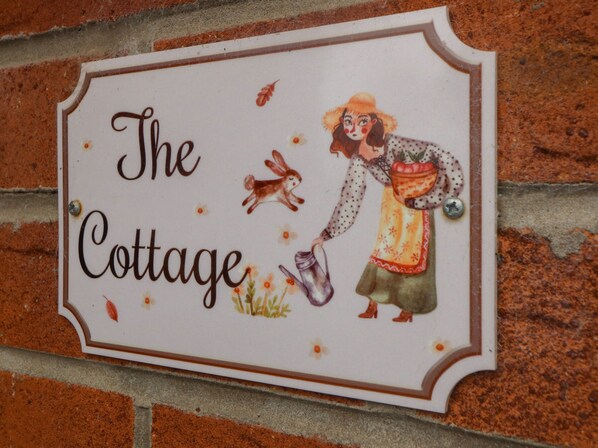 Une enseigne portant l’inscription « The Cottage » et illustrée d’une femme, d’un lapin et d’un arrosoir.