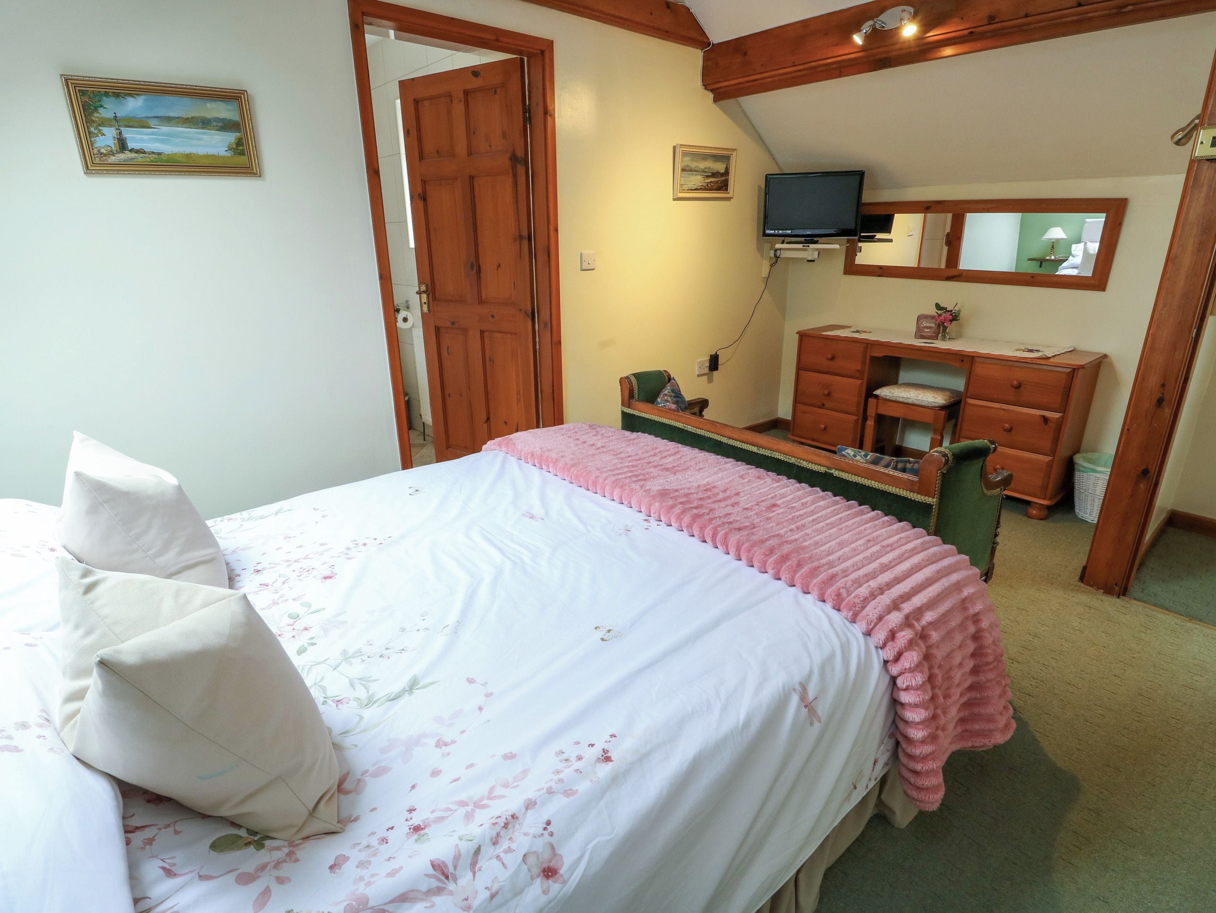 A bedroom with a bed, a dresser, a television, and a mirror.