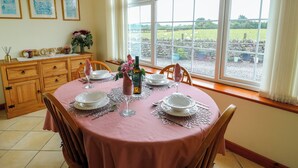 Een eetruimte met een tafel voor vier personen, een uitzicht op het landschap door grote ramen en een houten kast met lades.