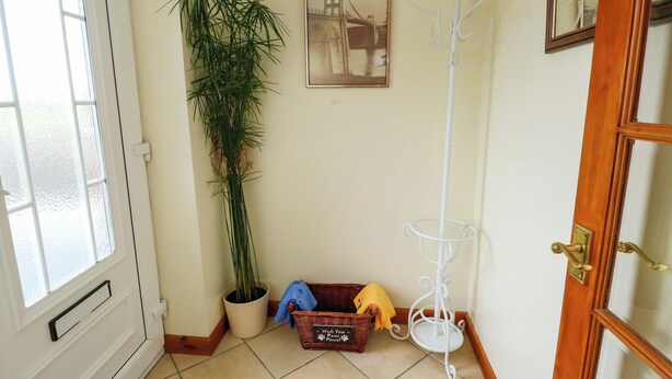 Een hoek van een kamer met een deur, een potplant, een lijst met een foto, een kapstok en een rieten mand met een bordje.