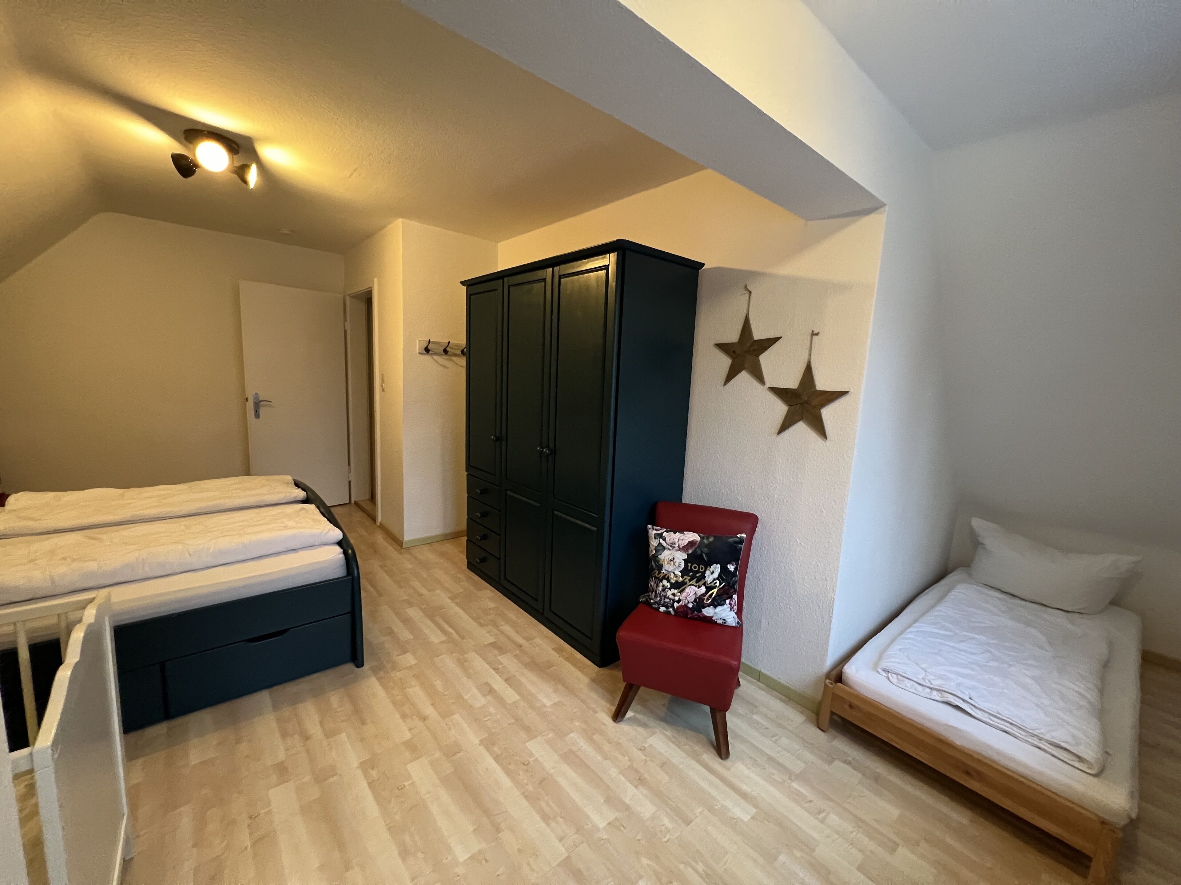A bedroom with two beds, a wardrobe, and a chair.