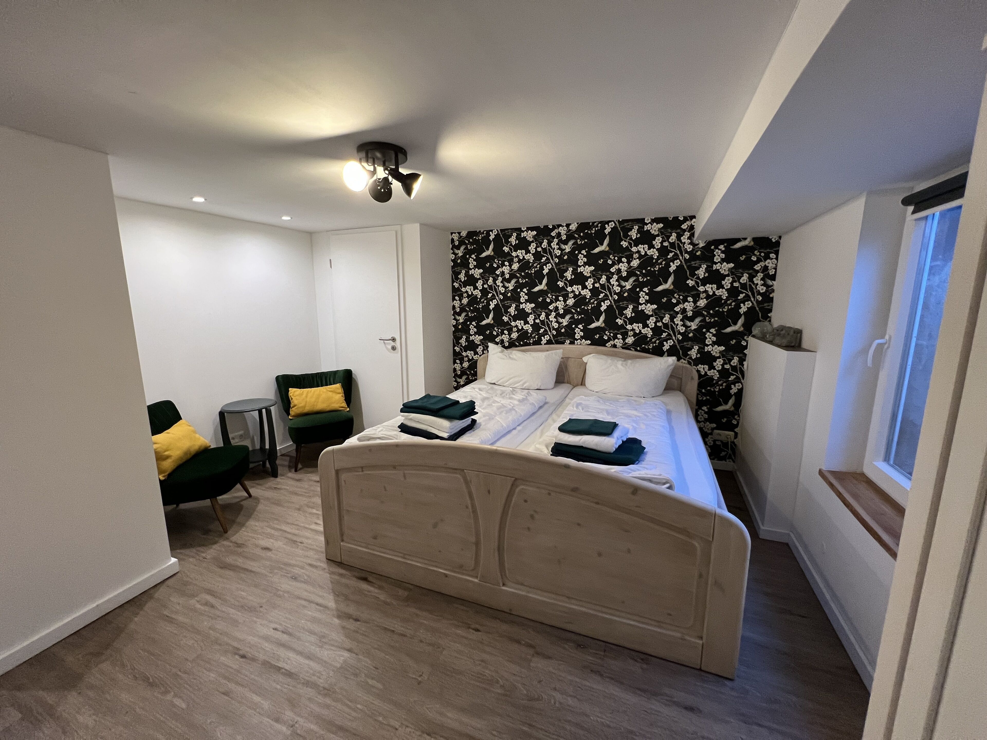 A modern bedroom with a bed, a chair, a small table, and a window.