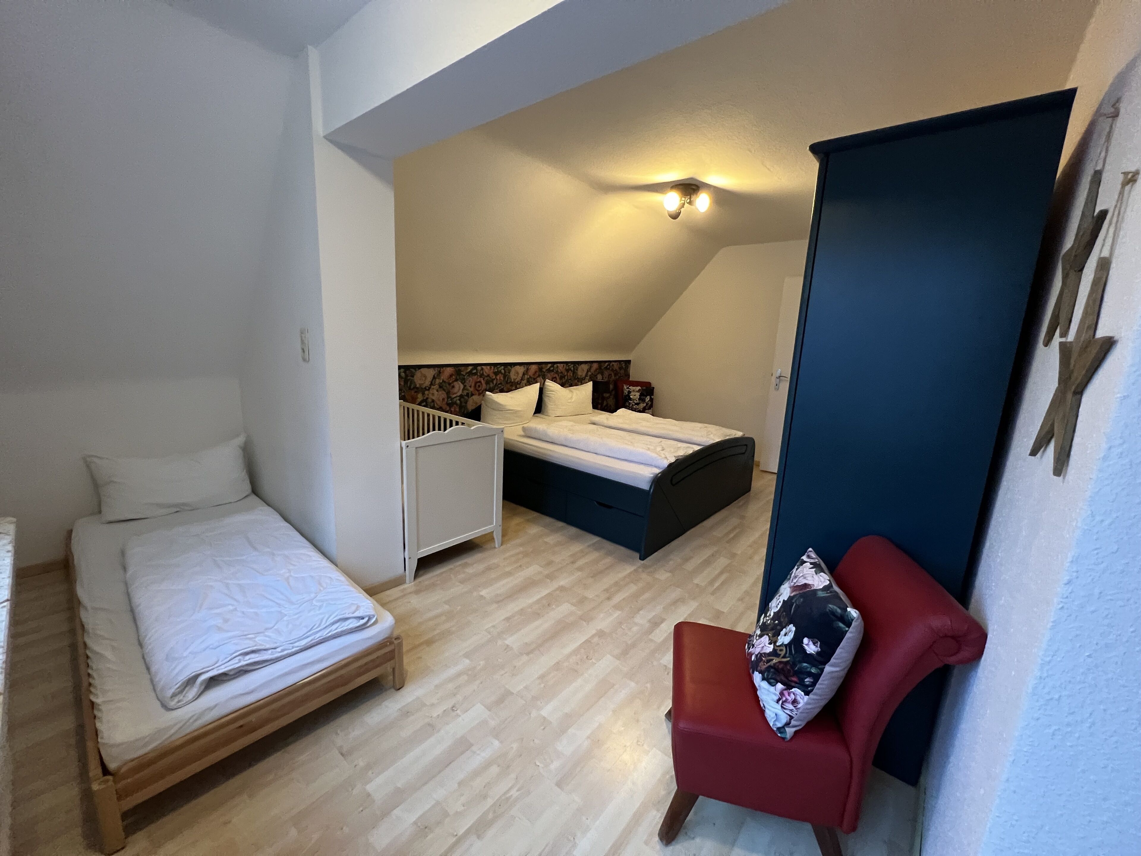 A bedroom with a wooden bed, a red chair, a small desk, and a white crib.