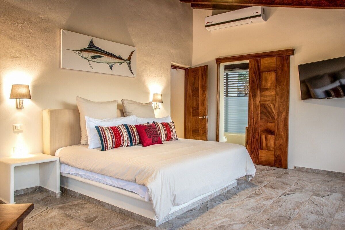 A bedroom with a bed, nightstands, a wall-mounted artwork of a fish, and a wooden door.