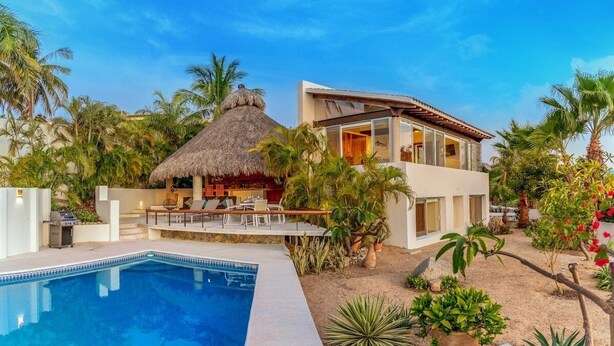 A modern villa with a pool, a thatched-roof structure, and lush tropical vegetation.